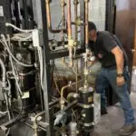 Copper refrigeration pipes, valves, and gauges beside a blue tank